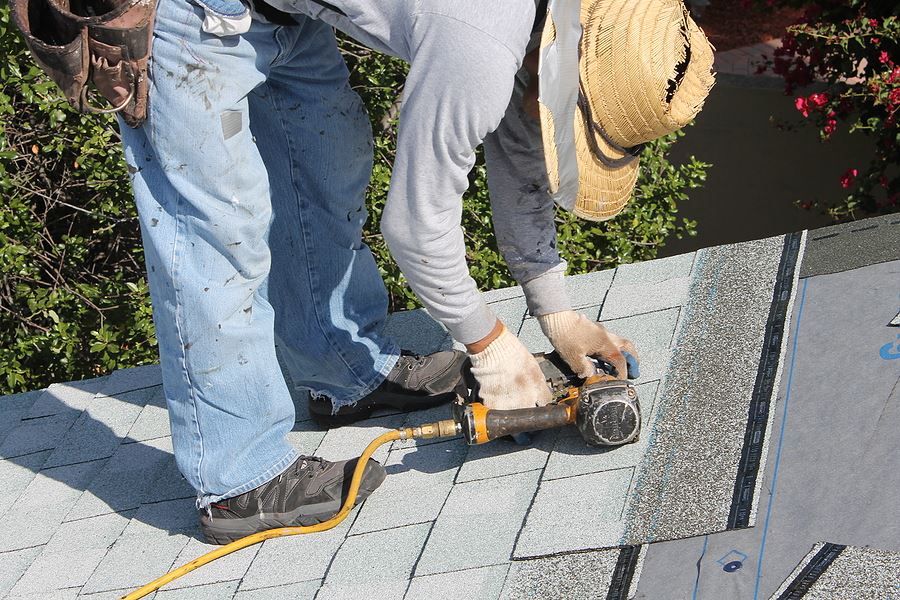 Construction worker leaning over hammering roof shingles